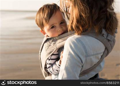Mother carrying baby. Mother with ergobaby carrying toddler on the beach