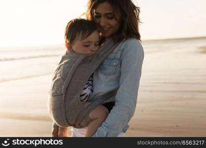 Mother carrying baby. Mother with ergobaby carrying toddler on the beach