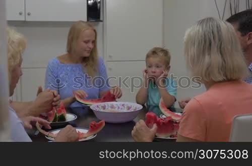Mother, child and grandparents eating tasty ripe watermelon in the dining room