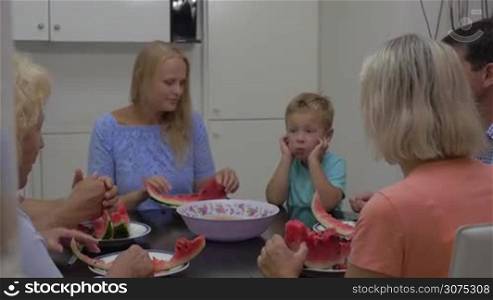 Mother, child and grandparents eating tasty ripe watermelon in the dining room