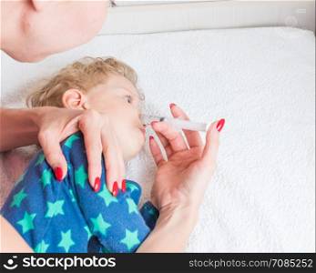Mother cleans the baby's nose with a syringe with saline water, while the infant is lying.