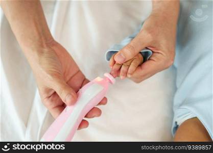 mother cutting newborn baby’s fingernails with auto electic nail trimmer.