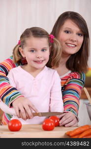 Mother cutting tomatoes with girl