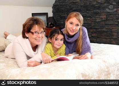 Mother, daughter and granddaughter reading book whilst laid on bed