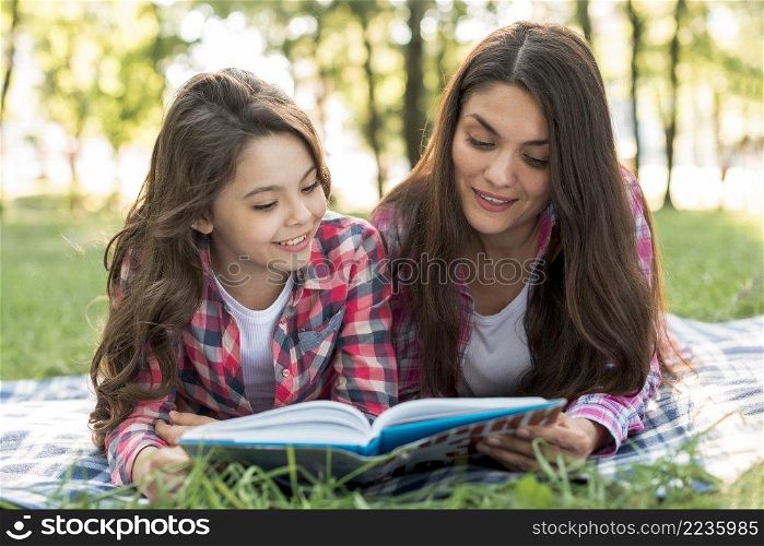 mother daughter lying blanket reading book together