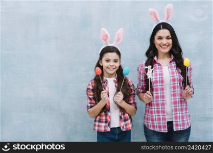 mother daughter wearing bunny ears holding easter eggs bunny props