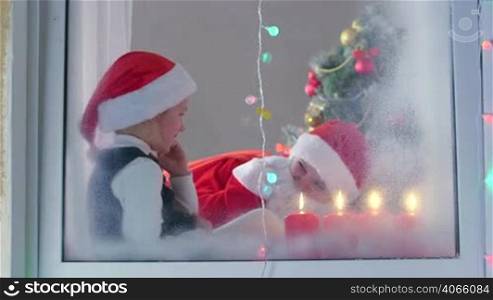 Mother dressed in a suit of Santa Claus with his little daughter celebrate Christmas at home
