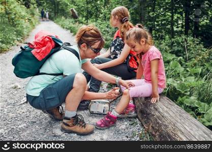 Mother dressing the wound on her little daughter’s knee with medicine in spray. Accident happened during family summer vacation trip. People actively spending time. Mother dressing the wound on her little daughters knee with medicine in spray. Accident happened during family summer vacation trip
