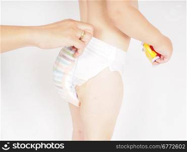 Mother dressing up toddler in diaper while standing, holding a yellow and red toy car