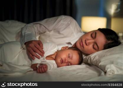 mother embraces the infant baby sleeping together in a bed at night