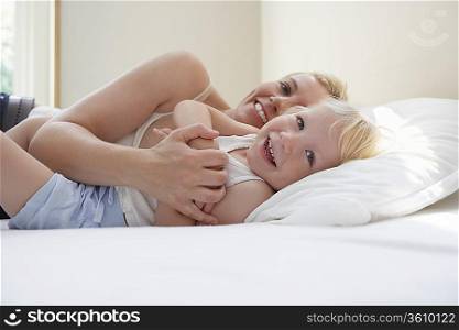 Mother embracing daughter (3-4) in bed smiling