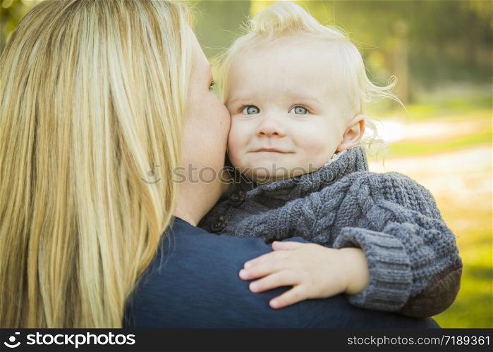 Mother Embracing Her Adorable Blonde Haired Blue Eyed Baby Boy Outdoors.