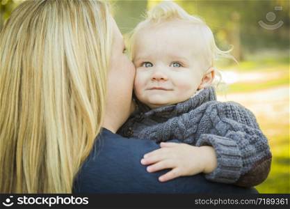 Mother Embracing Her Adorable Blonde Haired Blue Eyed Baby Boy Outdoors.
