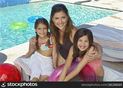 Mother embracing two daughters by swimming pool, portrait