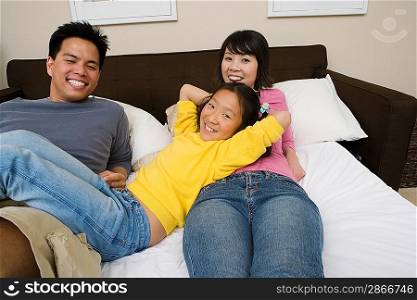 Mother, father and daughter lying down on bed and relaxing