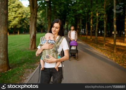 Mother, father and little baby walking along the alley in summer park. Mom and dad leisures with male kid, parents on picnic with child in the forest, family happiness. Mother, father and baby walking along the alley