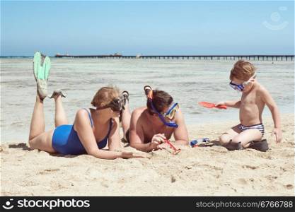 Mother, father and little son on summer vacation at the seaside, They wearing snorkels and flippers while lying and playing on the beach