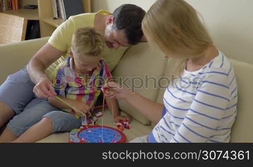Mother, father and little son playing electric fishing game at home. Indoor leisure with parents