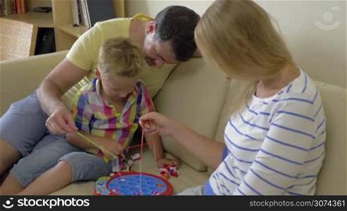 Mother, father and little son playing electric fishing game at home. Indoor leisure with parents