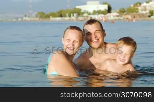 Mother, father and son bathing in sea on resort on a hot day. They having fun splashing water together. Family summer vacation