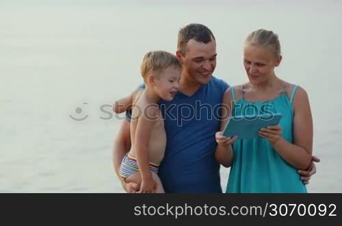 Mother, father and son by the sea looking at touch pad