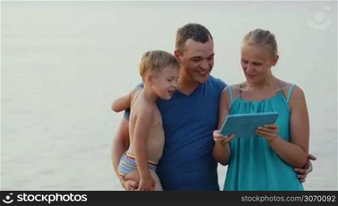 Mother, father and son by the sea looking at touch pad