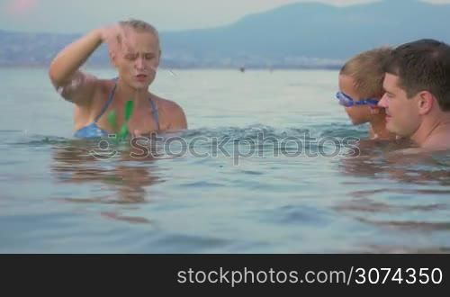 Mother, father and son having a good time while bathing in the sea. They playing with windup toy frog. Family fun on vacation