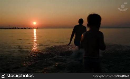 Mother, father and son running into sea to bathe at sunset
