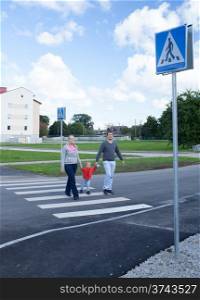 Mother, father and their little son crossing the road on crosswalk holding their hands.