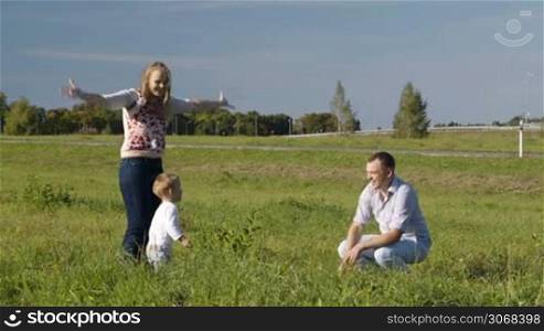 Mother, father and their little son having fun in the countryside. They throwing up grass, father kissing his wife and son.