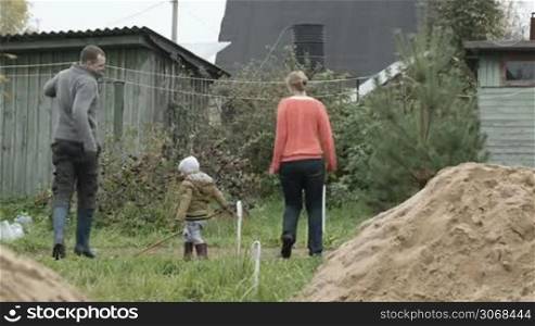 Mother, father and their little son having fun in the countryside. Parents dancing and boy playing with a long stick.