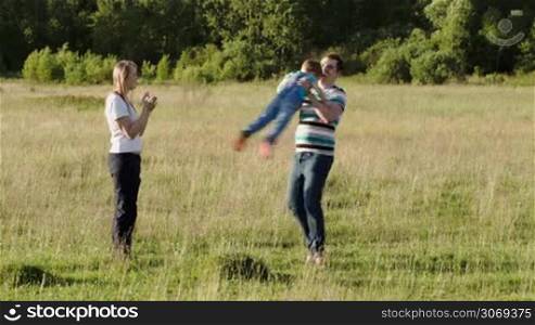 Mother, father and their son having fun on the meadow. Dad spinning the boy, then they running together