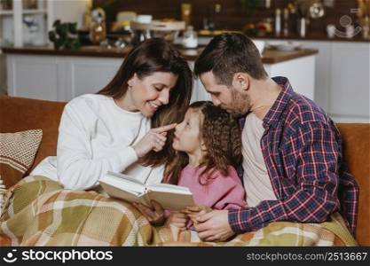 mother father reading book with daughter couch