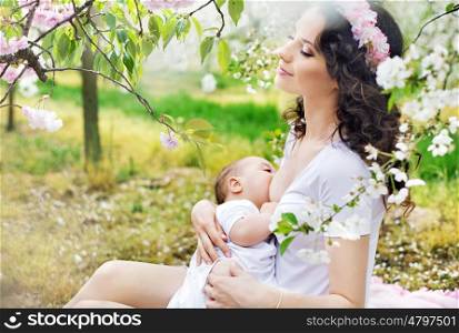 Mother feeding a baby in the spring orchard