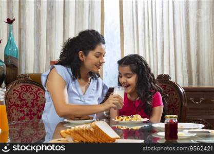 Mother Feeding a glass of milk to her daughter to during breakfast at home