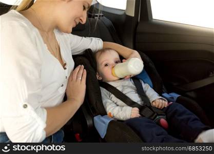 Mother feeding baby boy with milk on car back seat
