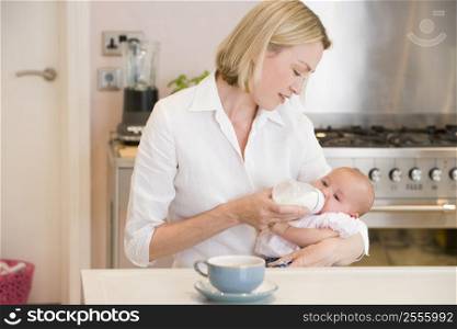 Mother feeding baby in kitchen with coffee