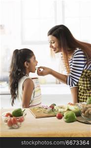 Mother feeding cucumber to daughter in kitchen