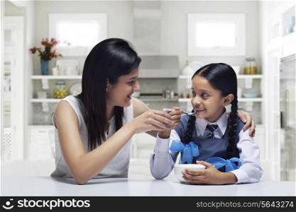 Mother feeding daughter breakfast at home