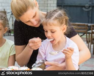 Mother feeding daughter with spoon confectionery glaze for cooking cakes