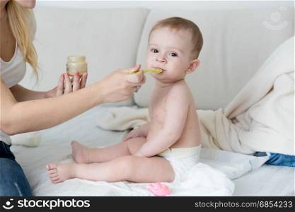 Mother feeding her baby boy with vegetable puree at bedroom