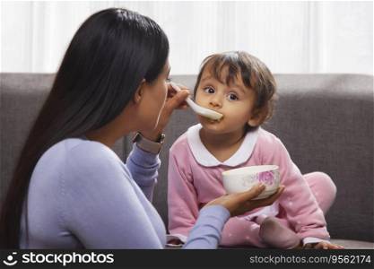 Mother feeding her baby with spoon in living room