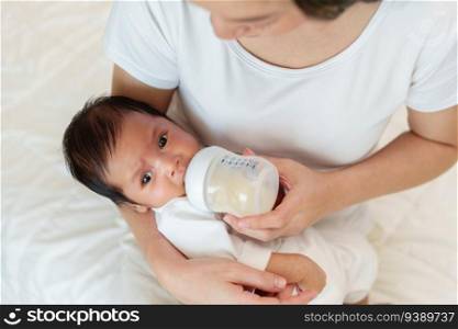mother feeding milk bottle to her newborn baby on a bed