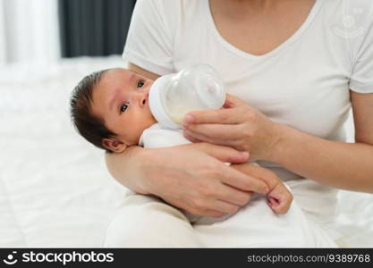 mother feeding milk bottle to her newborn baby on a bed