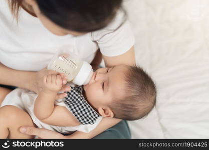 mother feeding milk from bottle and baby sleeping on a bed