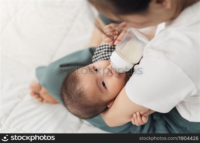 mother feeding milk from bottle and baby sleeping on a bed