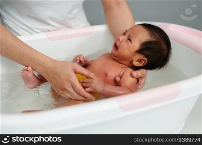 mother give a bath with crying newborn baby in a bathtub