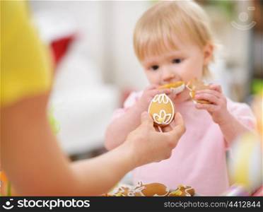 Mother giving baby cookie in shape of Easter egg. Focus on cookie
