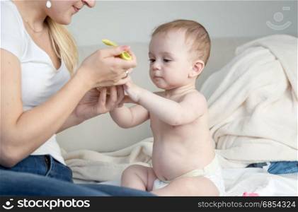 Mother giving soup to her baby son sitting on bed