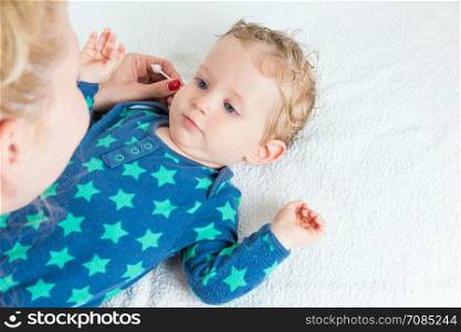 Mother hand cleaning baby ear with cotton swab,infant lying with wet hair and blue eyes,copy space,horizontal photo.